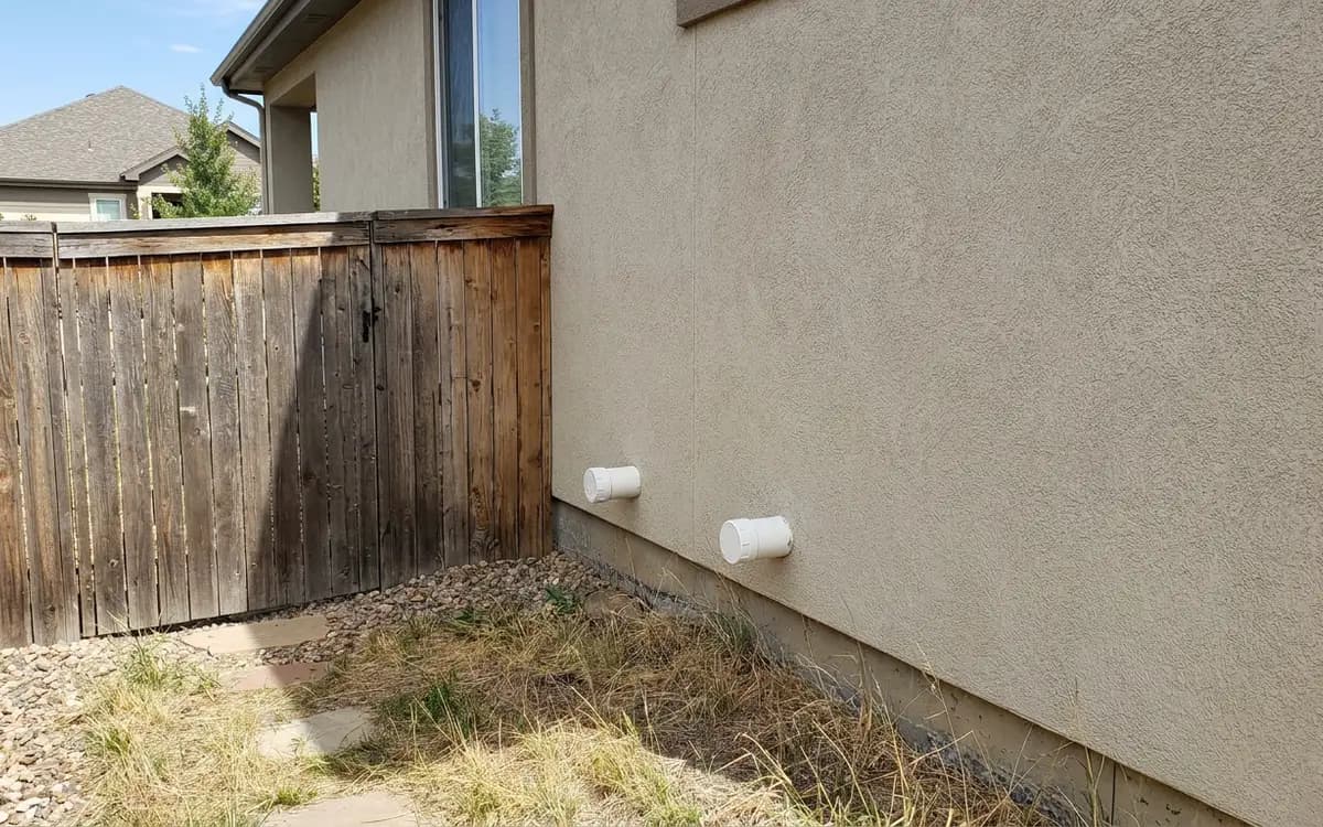 Plain capped white furnace vent terminations on the side of a newer stucco home