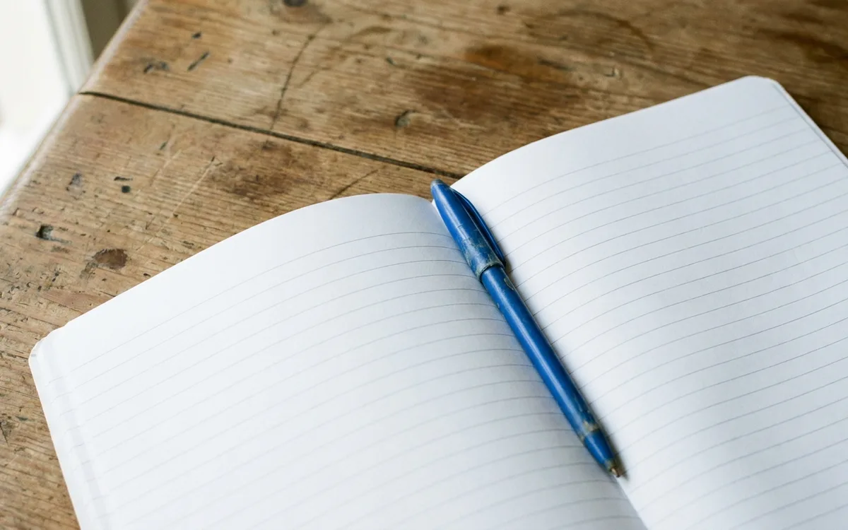 Two blank sheets of paper side by side on a kitchen table with a pen