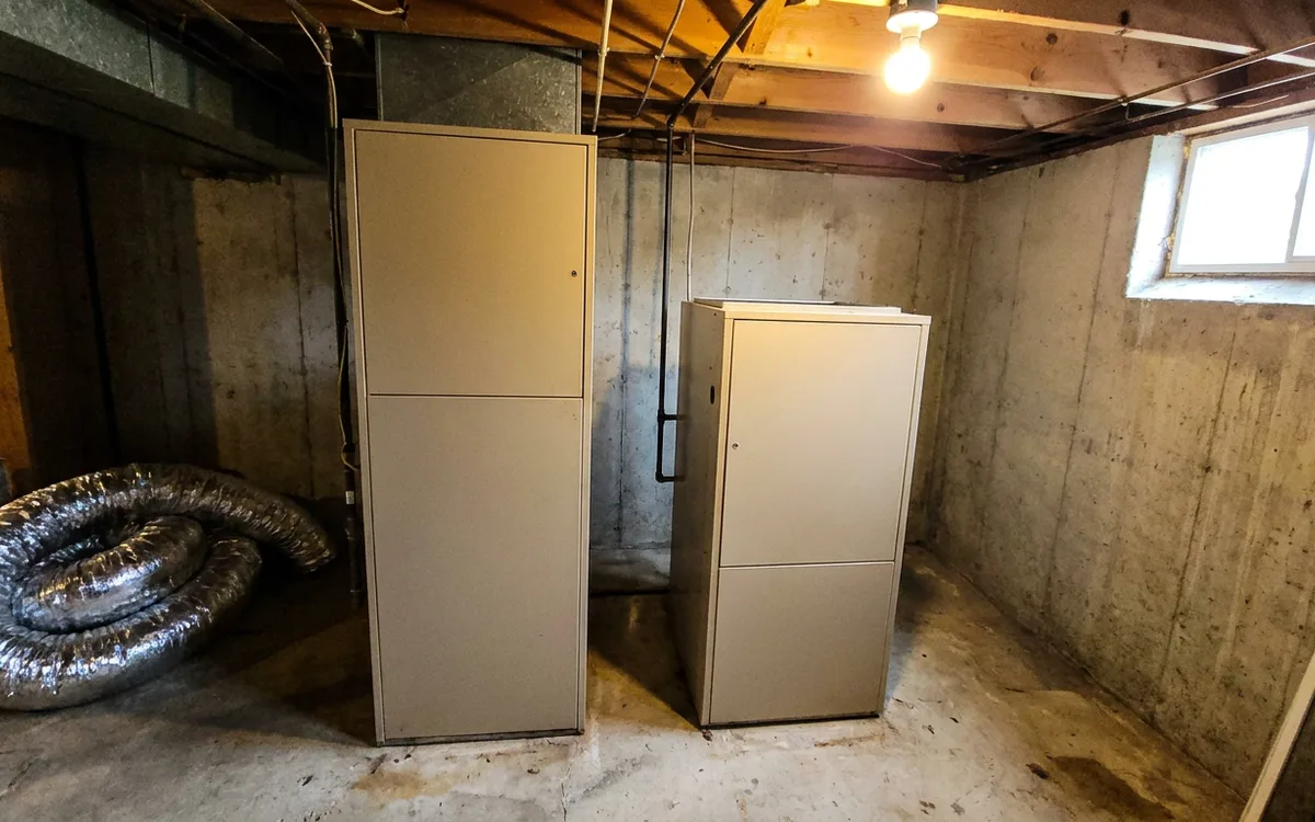 Two gas furnace cabinets of different heights standing side by side in a basement