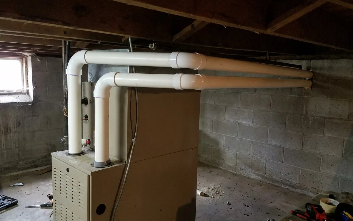 New white PVC flue piping routed through a basement rim joist